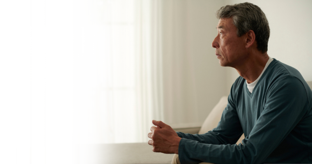 Man in a teal sweater looking out a window, reflecting on a new diagnosis in the family